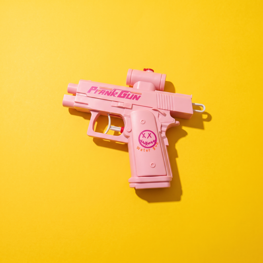 Pistola de agua de broma rosa con la inscripción PRANK GUN, sobre fondo amarillo