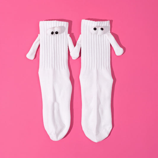 Par de calcetines blancos con ojos saltones y bracitos con imán que se dan la mano, sobre fondo rosa